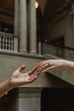 two people reaching out their hands to each other in front of a building with columns