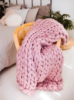 a pink blanket sitting on top of a bed next to a basket filled with pillows