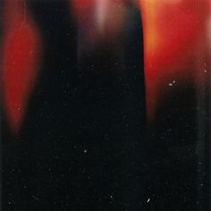 blurry photograph of red and black vases with one candle in the middle, against a black background