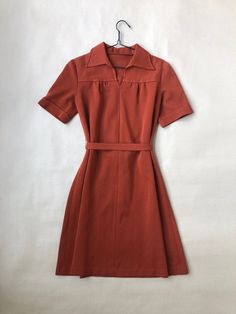 a red dress hanging on a white wall with a hanger in front of it