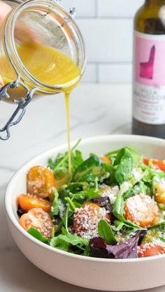 someone pouring dressing into a salad in a bowl