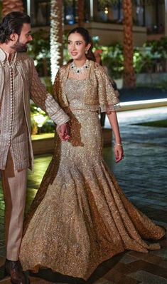 a man and woman dressed in formal wear walking down the street at night with palm trees behind them