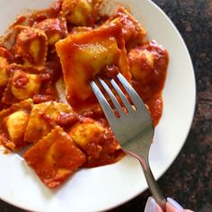 a person holding a fork over a plate of ravioli with sauce and cheese on it