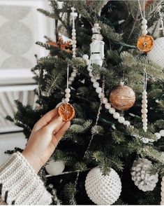 a woman is decorating a christmas tree with ornaments and oranges on the branches