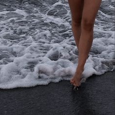 a woman walking on the beach with her bare feet in the water and waves coming ashore