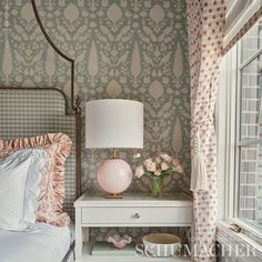 a bedroom with pink and white decor on the nightstand next to the bed in front of the window