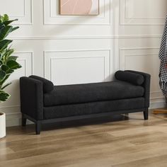 a living room with a black couch next to a potted plant on the floor