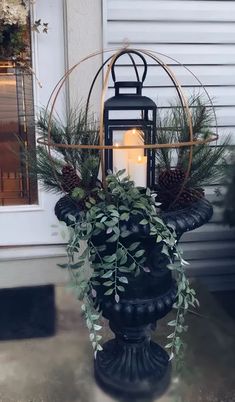 a candle is lit in a black urn with greenery and pine cones on it