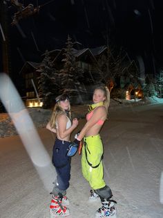 two women standing in the snow with skis on their feet and one holding onto her leg