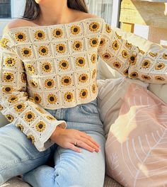 a woman is sitting on a couch with her hands in her pockets and wearing a sunflower sweater