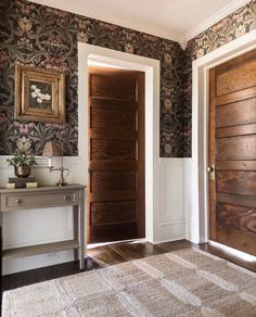 two wooden doors in a room with floral wallpaper and rugs on the floor