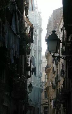 an alley way with clothes hanging from the buildings and street lamps on either side,