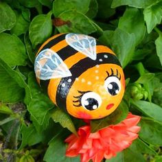 a painted bee sitting on top of a red flower next to green leaves and plants