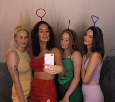 four women standing next to each other in front of a wall holding up cell phones