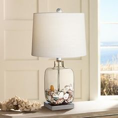 a lamp that is sitting on a table next to some rocks and sea shells in a glass jar