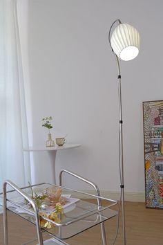 a living room with a glass table and metal chair next to a large lamp in the corner