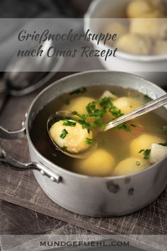 a pot filled with soup and dumplings on top of a wooden table next to spoons