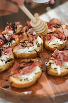 a wooden plate topped with mini sandwiches covered in toppings