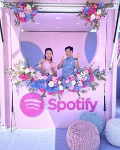 two people standing in front of a spotify sign with flowers on the wall behind them