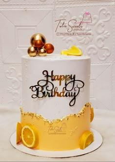 a birthday cake decorated with gold and white icing, lemon slices and the words happy birthday written on it