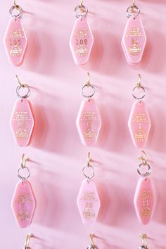 pink and gold keychains with words on them hanging from hooks against a pink background