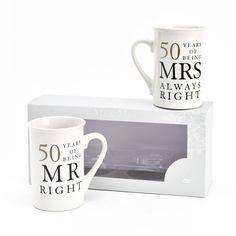 two coffee mugs sitting next to each other in front of a boxed gift box