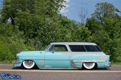 an old car is parked on the side of the road in front of some trees