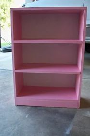 a pink bookcase sitting in the middle of a room next to a white car