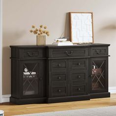 the sideboard is black with glass doors and drawers on it's sides, in front of a beige wall