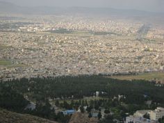 an aerial view of a city with lots of trees in the foreground and mountains in the background