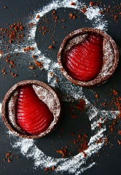 two desserts with powdered sugar and red fruit in the middle on a black surface