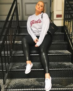 a woman is sitting on the steps wearing black leggings and a grey sweatshirt