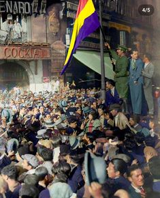 a crowd of people standing around each other in front of a building with a flag