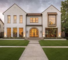 a large white house with lots of windows and grass in the front yard at dusk