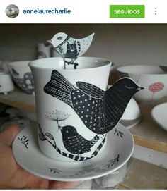 a hand holding a coffee cup and saucer with two birds on the top of it