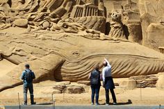 two people are standing in front of a large sand sculpture that looks like a whale