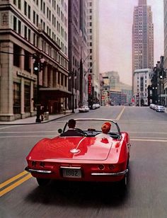 an orange convertible car driving down a street next to tall buildings with flowers on it