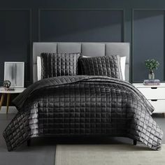 a bed with black comforter and pillows on top of it in a gray room