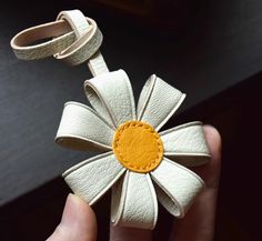 a hand holding a white leather flower with yellow center and brown center on the petals