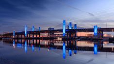 a bridge that is over some water with blue lights on it and the sky in the background