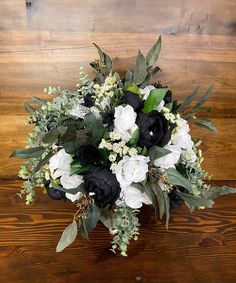 a bouquet of white and black flowers sitting on top of a wooden table next to a wall