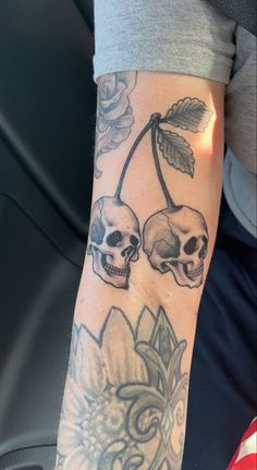 a person with a tattoo on their arm holding a flower and two skulls in the background