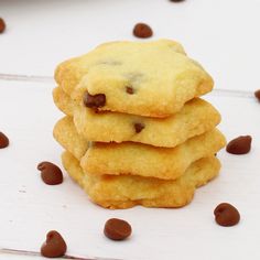 a stack of chocolate chip cookies on top of a white table with scattered chocolate chips