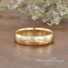 a gold wedding band with leaves engraved on the side, sitting on a wooden surface