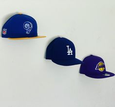 three new era hats are hanging on the wall in front of each other, including one los angeles dodgers cap