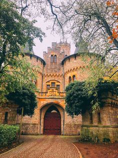 an old castle with a red door and brick walkway leading to the front entrance is surrounded by trees