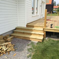 a wooden deck next to a white house and pile of wood on the ground in front of it