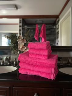 a stack of pink towels sitting on top of a bathroom sink next to a mirror