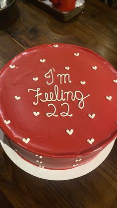 a red cake sitting on top of a table with white hearts around it and the words i'm feeling 22