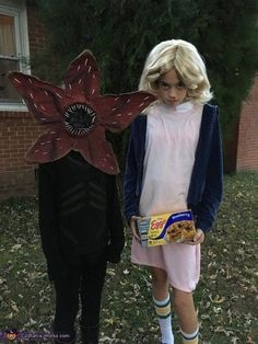 two children dressed up in costumes standing next to each other on the grass with one holding a box of cereal